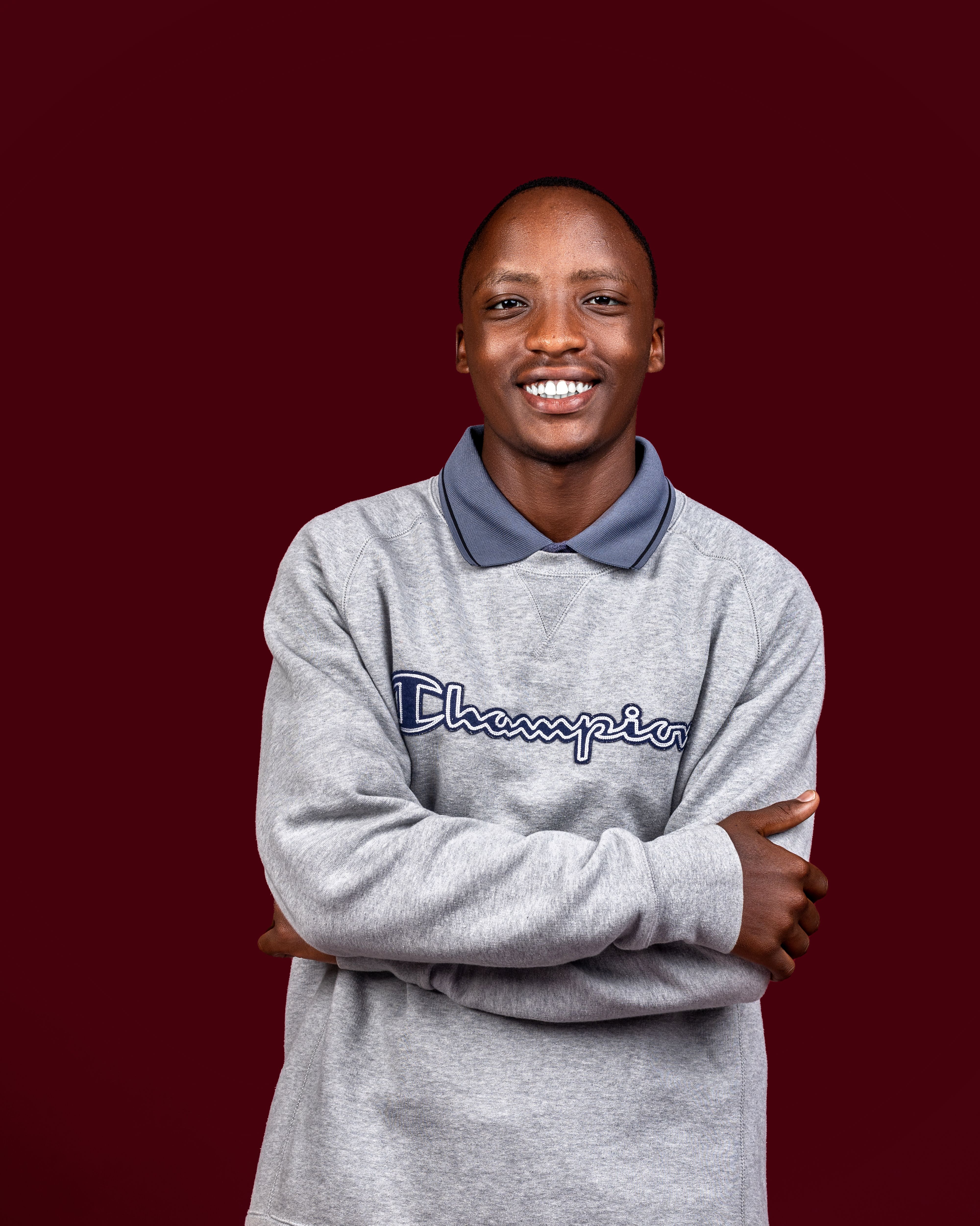 Confident young man smiling in casual grey sweater against a maroon background