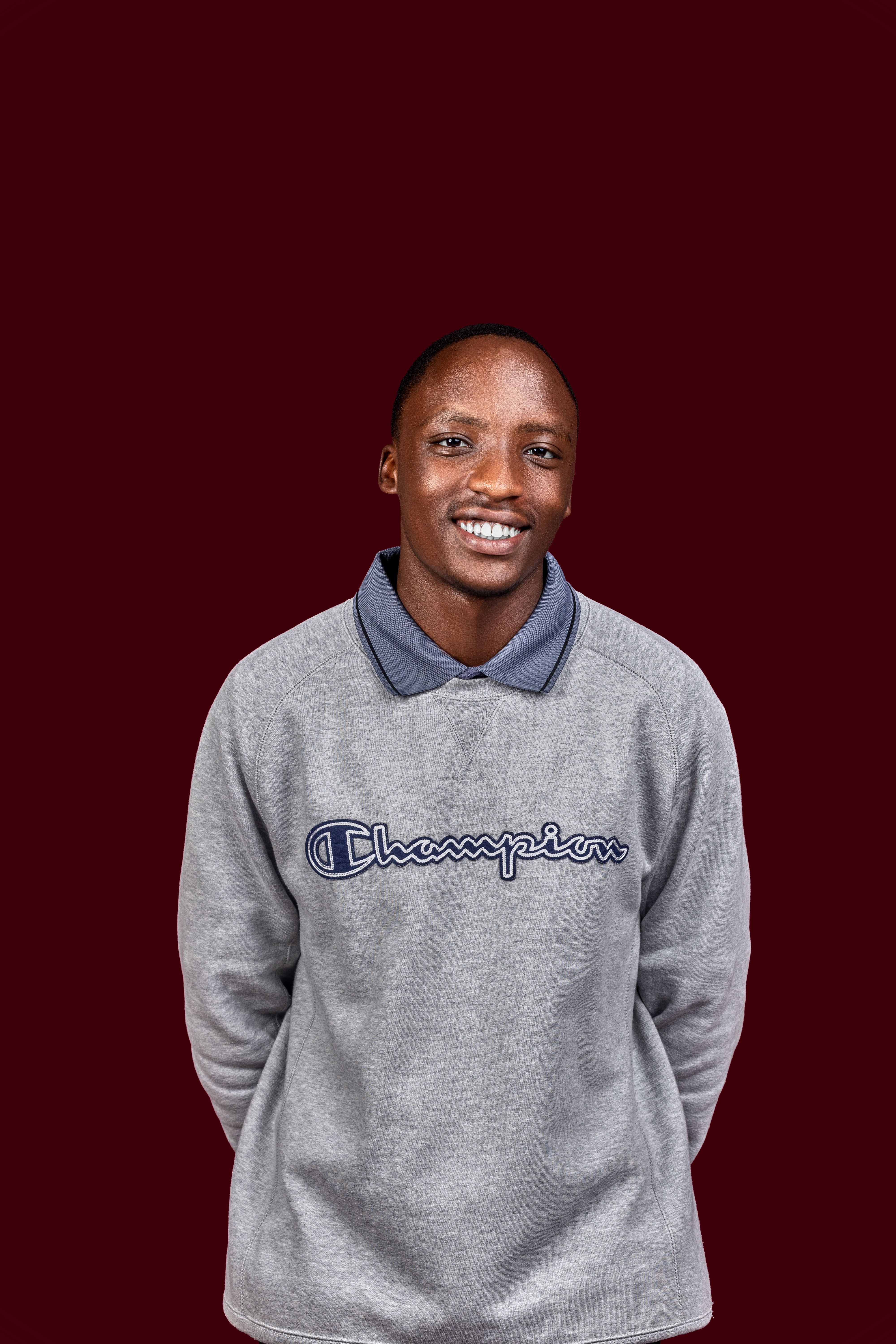 A cheerful individual posing in a grey Champion sweatshirt against a dark background.