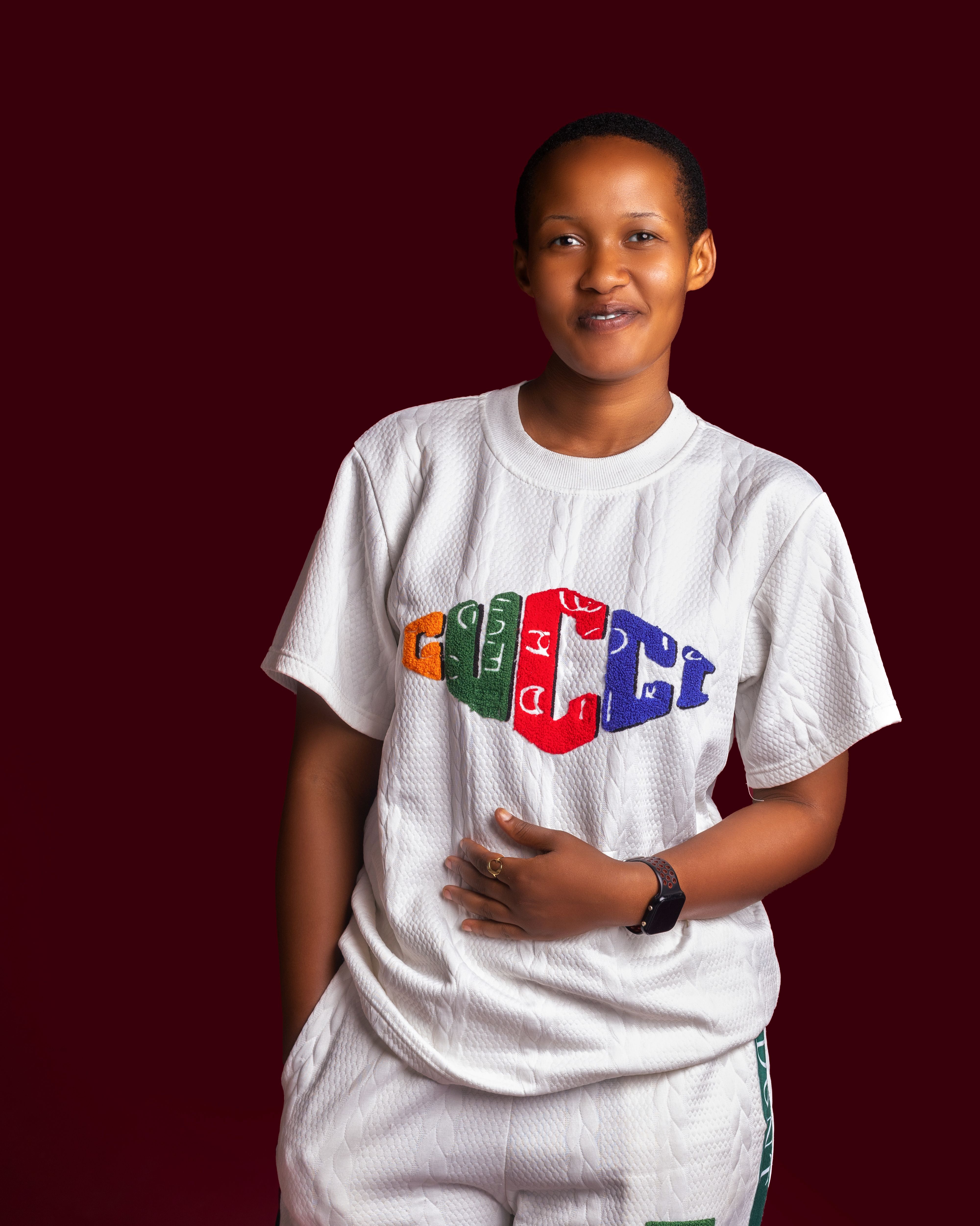 Smiling African woman wearing a colorful logo white shirt on a maroon background.