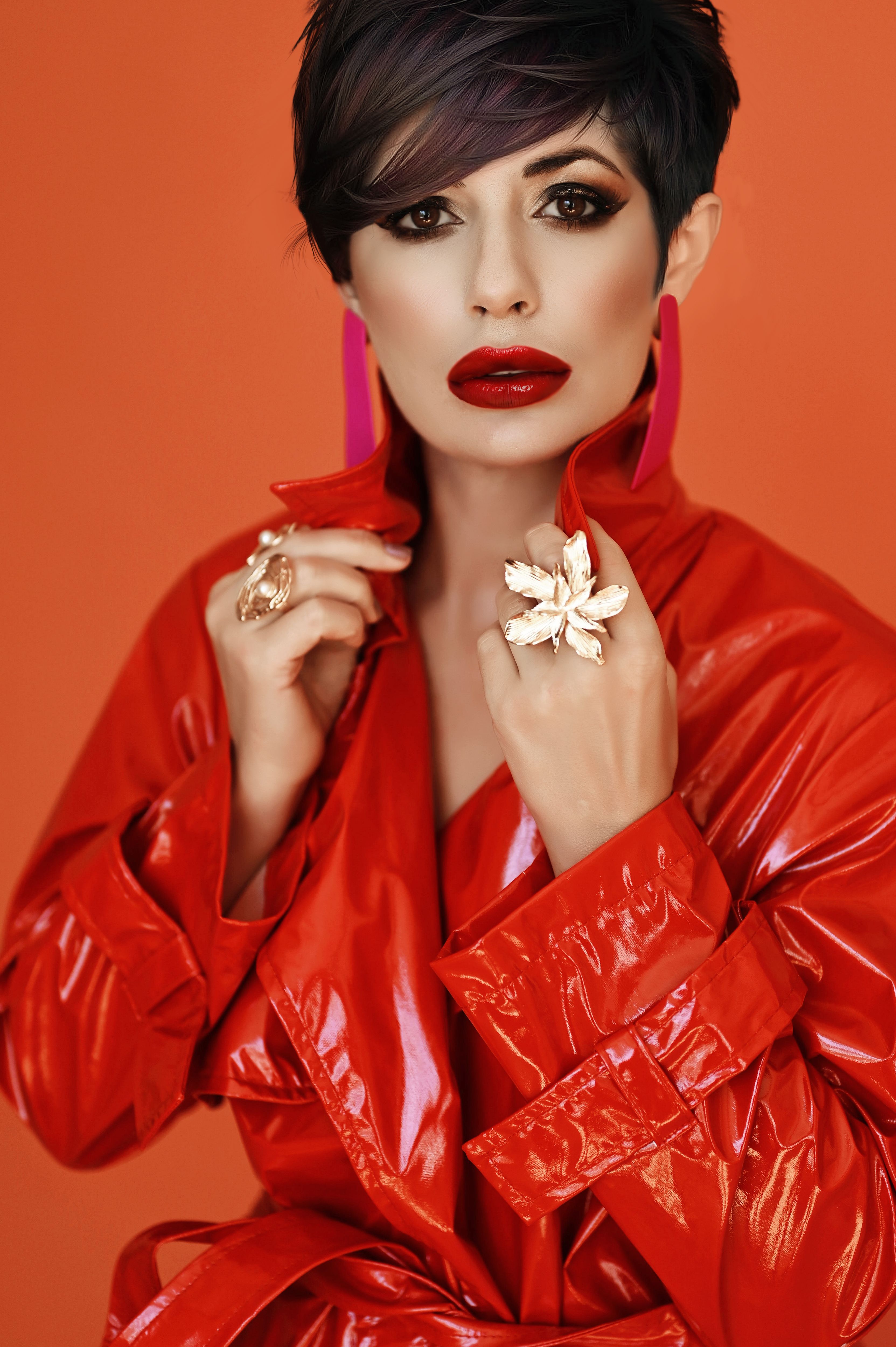 A stylish woman with red lips and striking rings poses in a vibrant red coat.