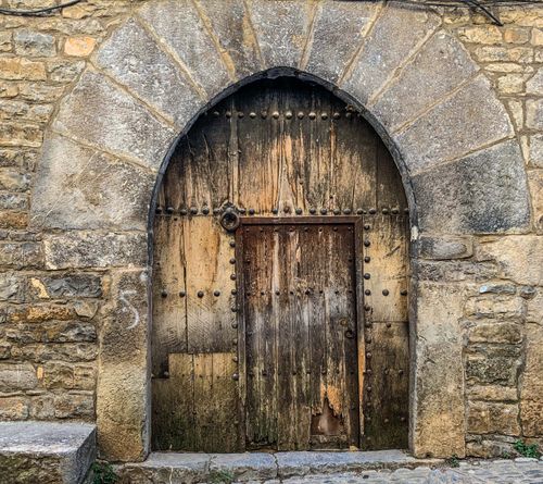 Free Weathered wooden door set in an aged stone wall with arch design. Stock Photo