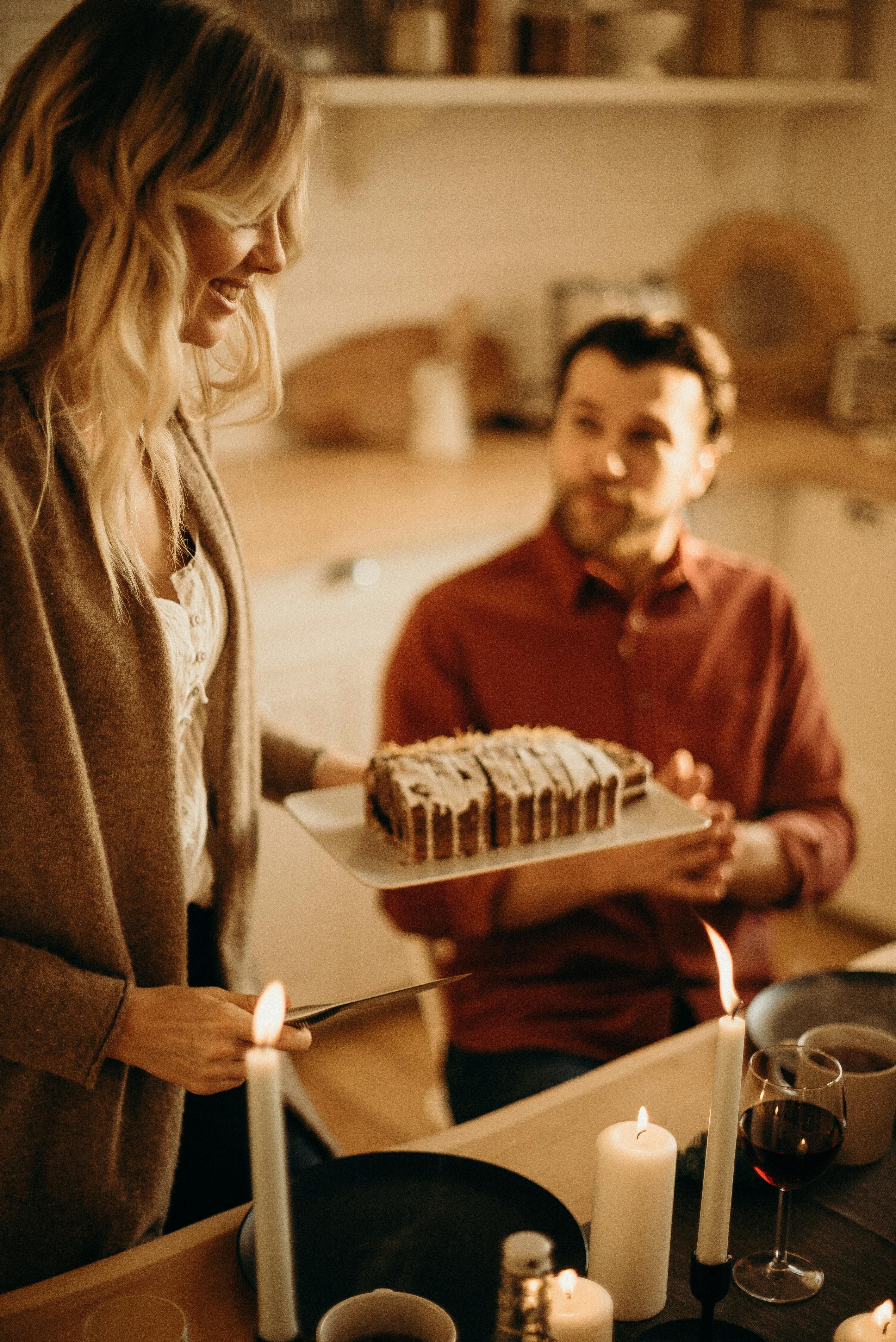 Woman standing while serving cake and the man sitting near a table. | Photo: Pexels