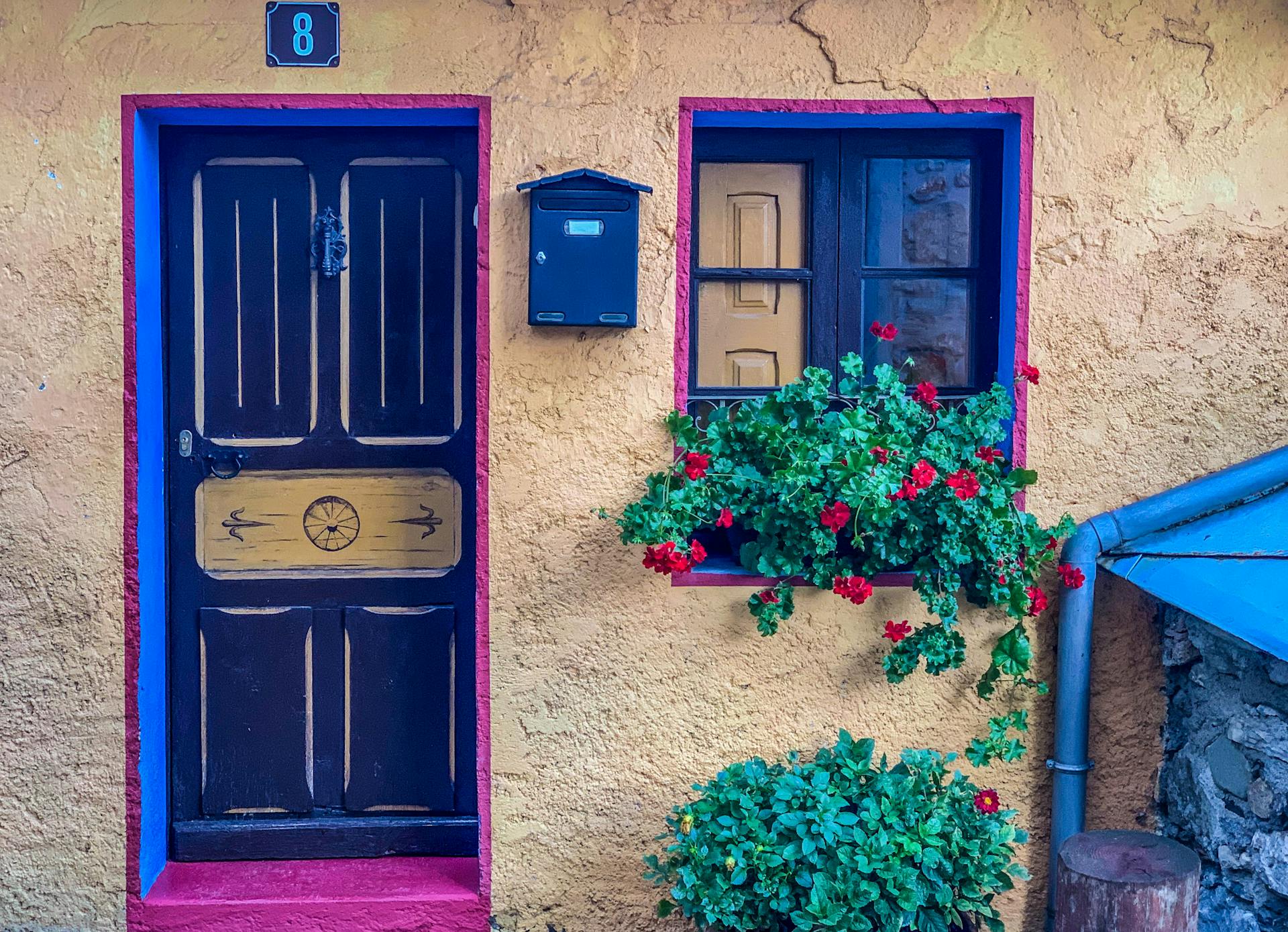 Charming vibrant house facade with colorful door, window flowers, and mailbox.