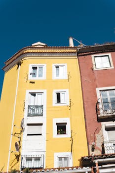 Bright yellow and red facades of Lisbon apartments under a clear blue sky.