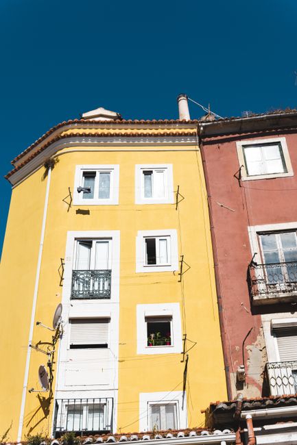 Bright yellow and red facades of Lisbon apartments under a clear blue sky.