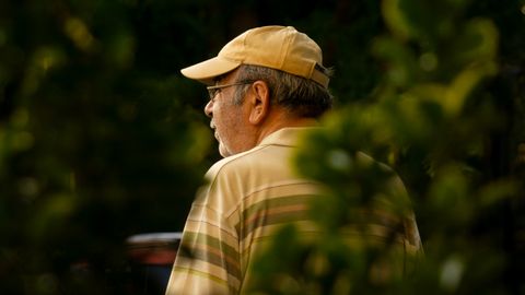 Senior man wearing a cap surrounded by greenery, enjoying a peaceful moment in nature.