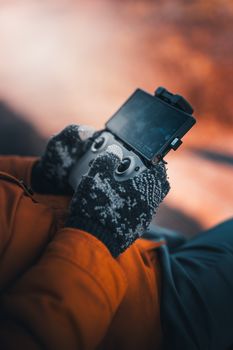 A close-up of hands in gloves controlling a drone with a remote controller in a moody outdoor setting.
