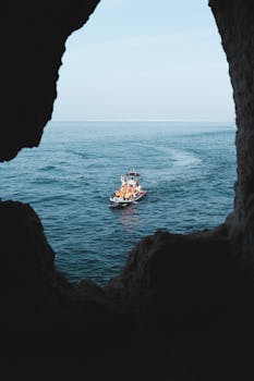 A boat navigates through the tranquil waters of the ocean as seen from a cave in Carvoeiro, Portugal.