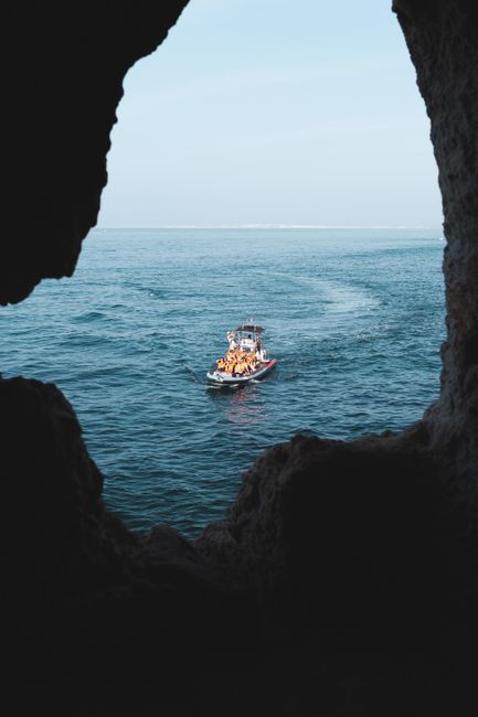 A boat navigates through the tranquil waters of the ocean as seen from a cave in Carvoeiro, Portugal.