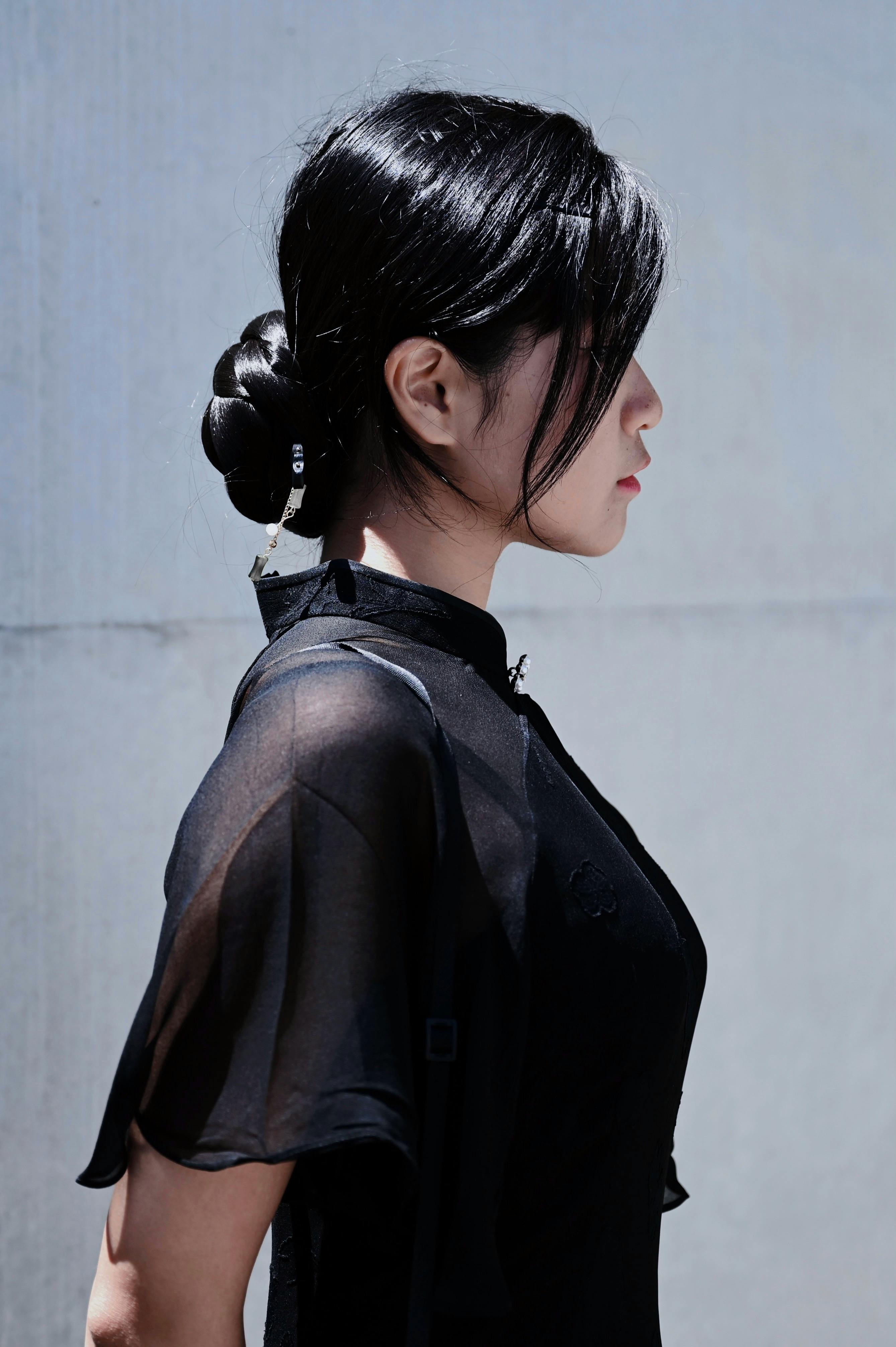 Profile of a woman in elegant black attire and hair bun, captured outdoors.