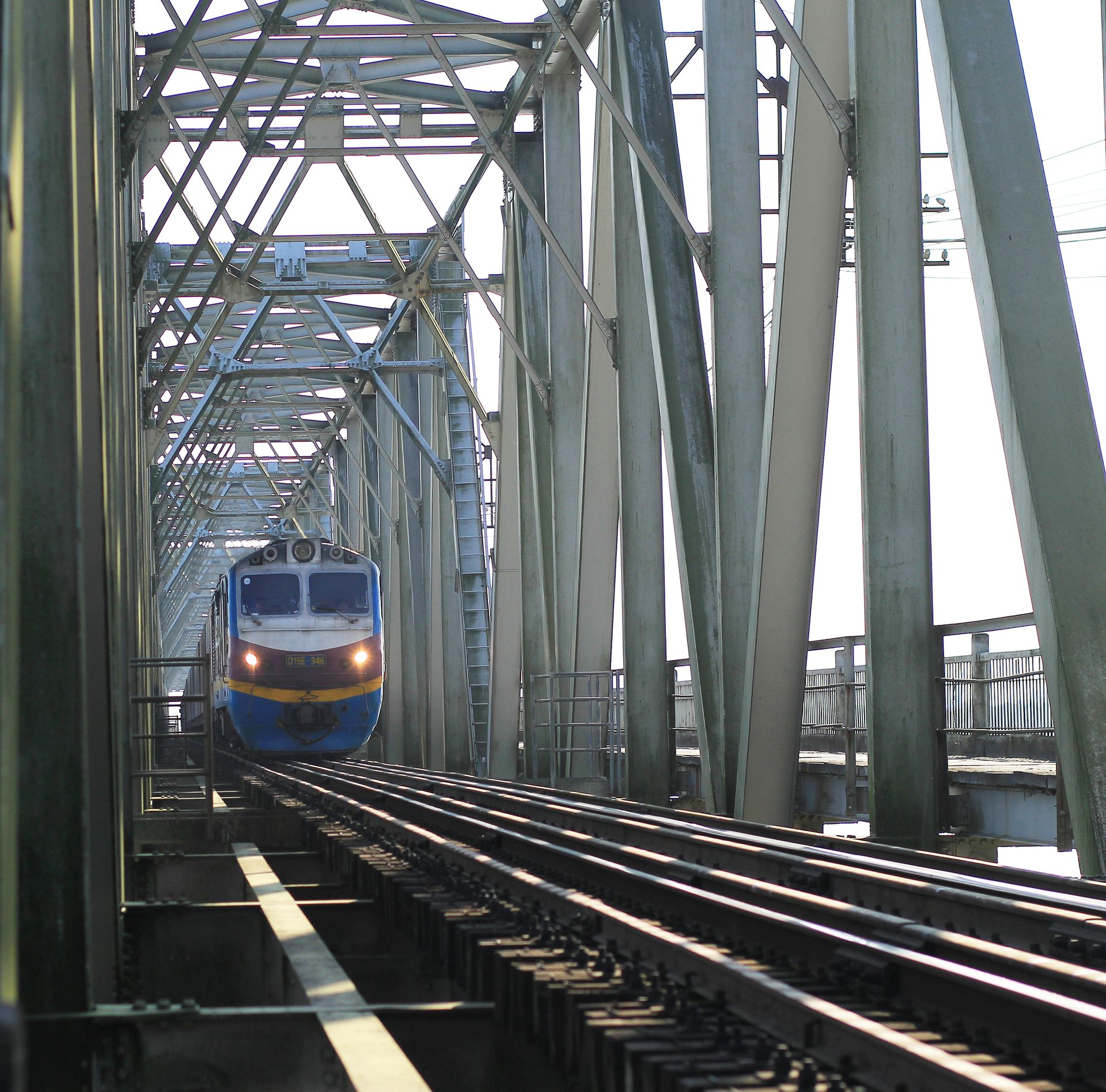 A train crosses a steel bridge under bright daylight, showcasing engineering and travel.