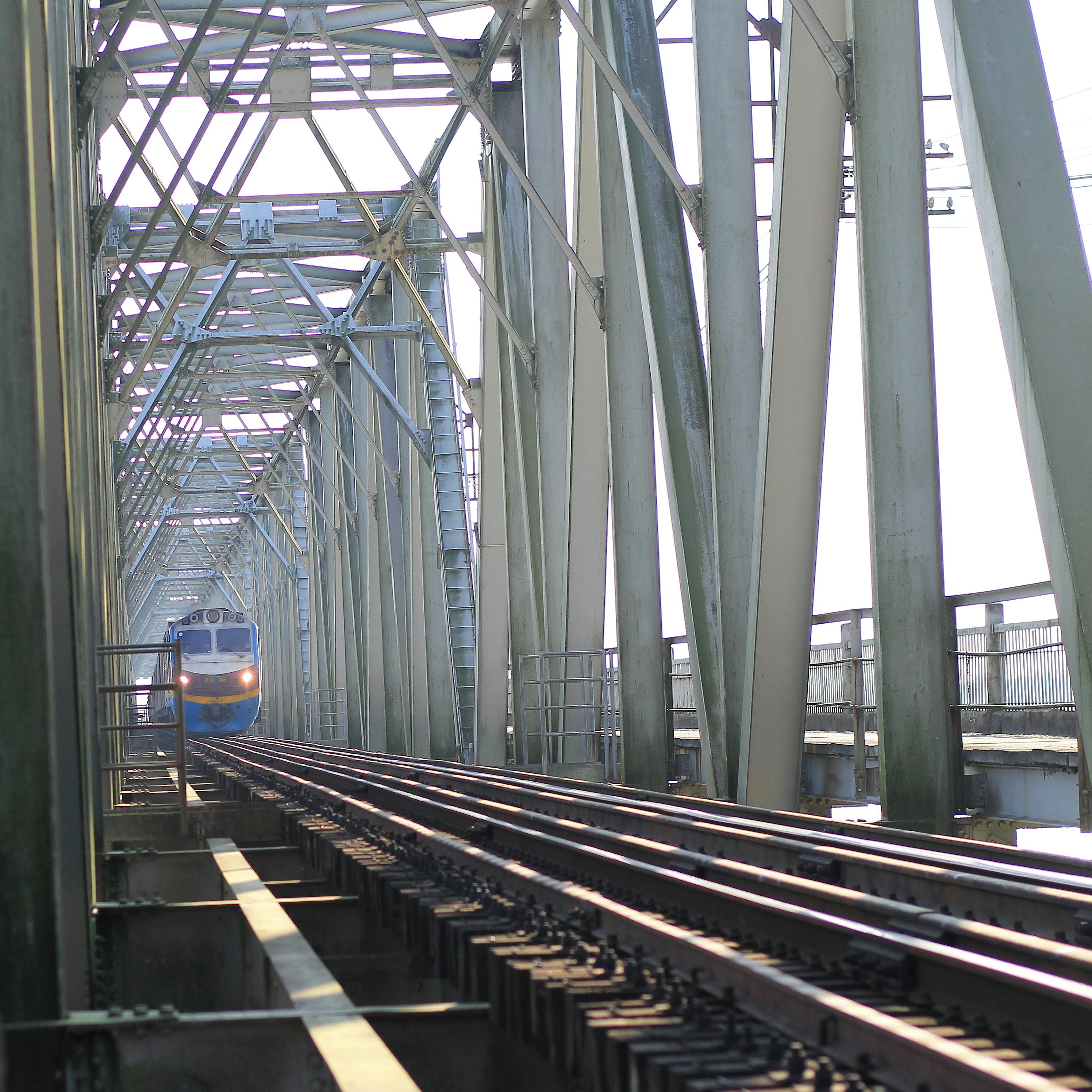 A train travels across a large steel truss bridge under bright daylight, showcasing engineering and transportation.