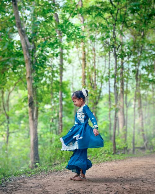 Free A young girl in traditional dress dances joyfully in a sunlit forest clearing. Stock Photo