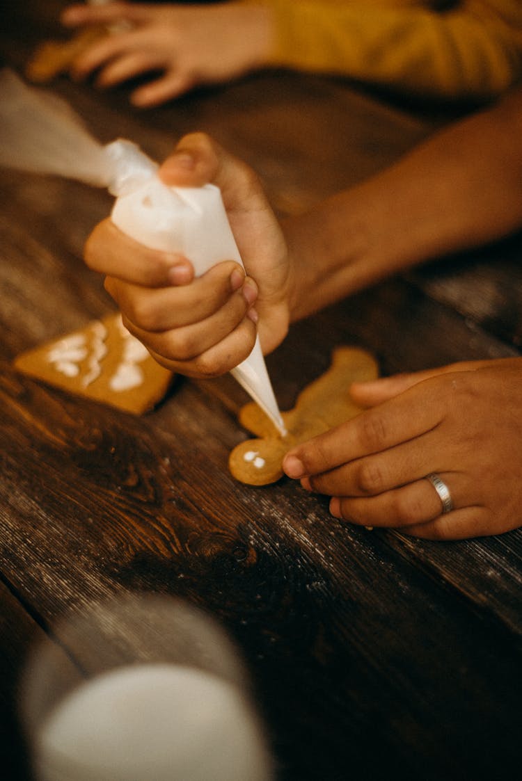 Person Piping Icing On Gingerbread Cookie