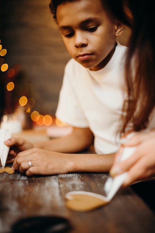 Boy Watching Another Kid Putting Icing on Cookie