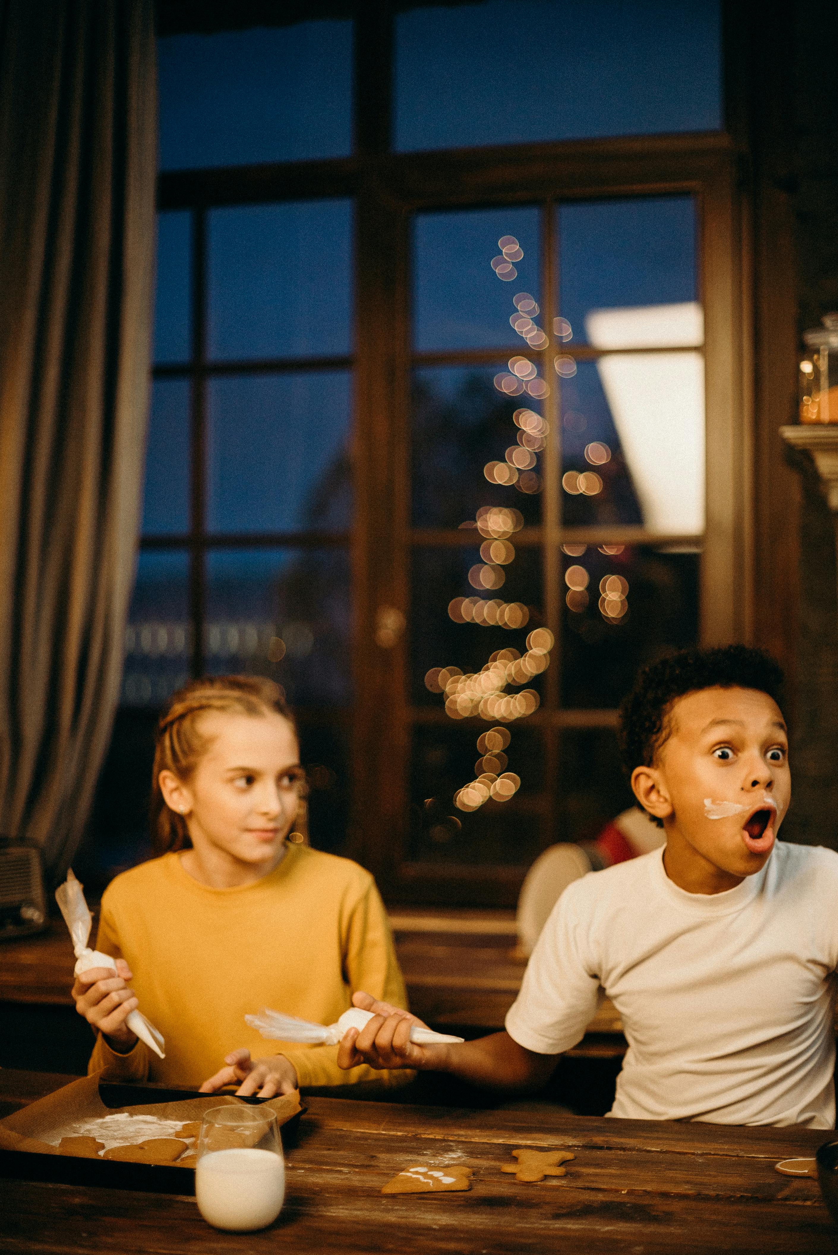两个孩子在室内装饰圣诞饼干，玩得很开心，有趣的表情和节日气氛都被捕捉到了