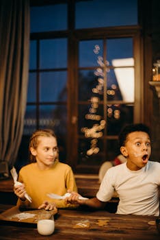 两个孩子在室内装饰圣诞饼干，玩得很开心，有趣的表情和节日气氛都被捕捉到了