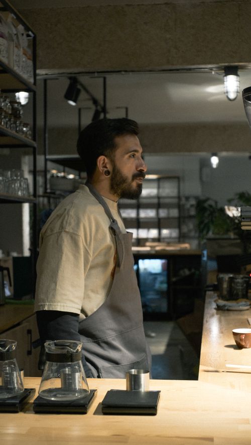Free A barista in an apron prepares a drink in a warm, cozy café with industrial decor. Stock Photo