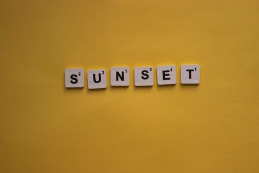 Scrabble tiles on a vibrant yellow background spell out the word 'Sunset', creating a minimalist design.