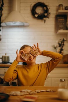 一个开朗的女孩在舒适的厨房里，开玩笑地拿着心形圣诞饼干