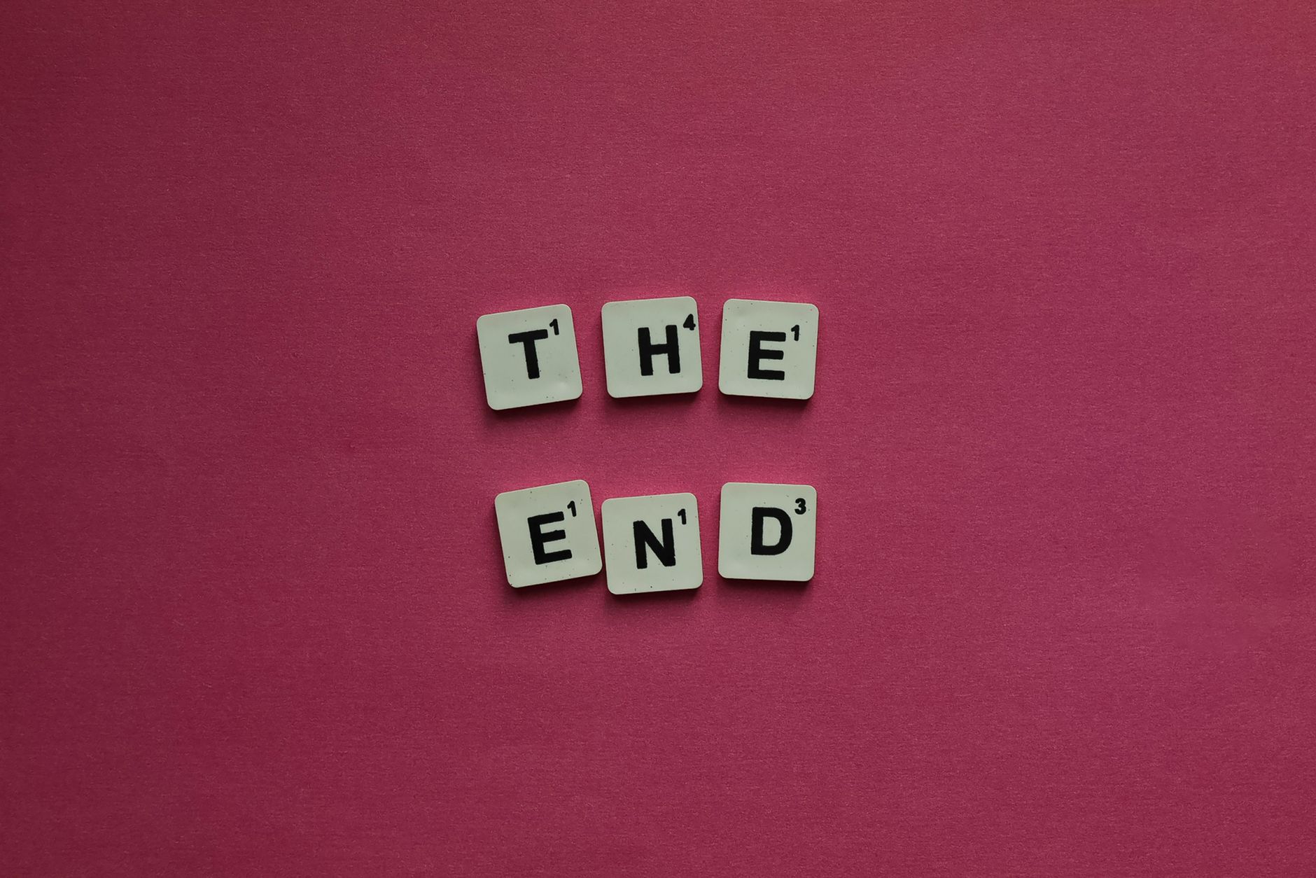 Scrabble tiles spell 'The End' against a vibrant pink background, symbolizing conclusion.