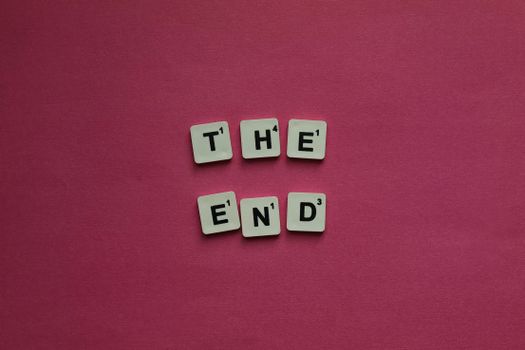 Scrabble tiles spell 'The End' against a vibrant pink background, symbolizing conclusion.