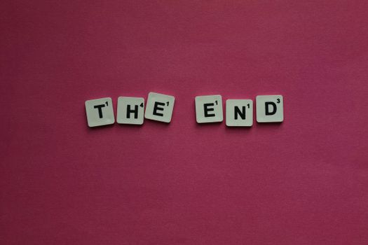 Scrabble letters spell 'The End' on a vibrant pink background.