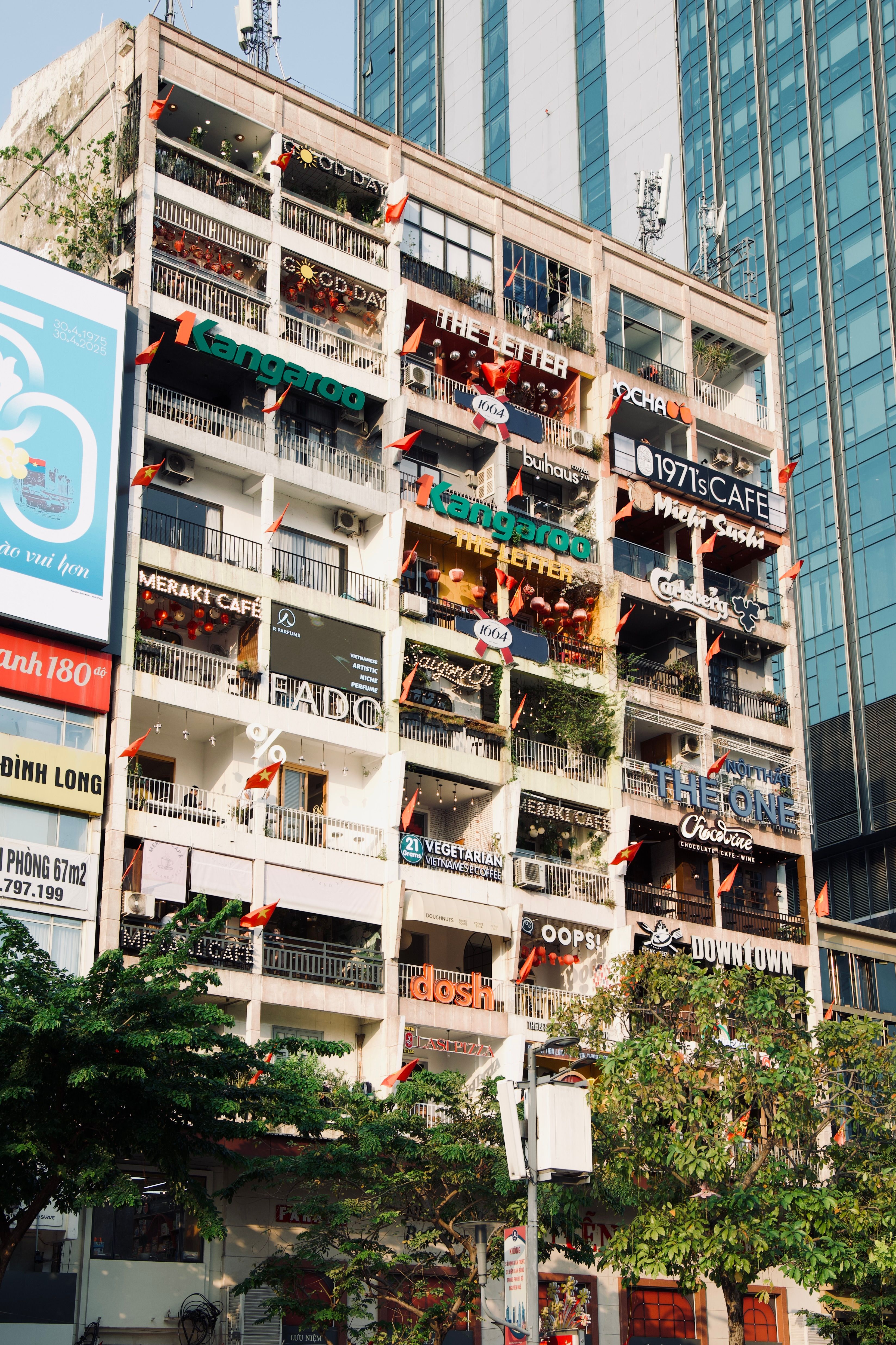 Colorful apartment building facade in Ho Chi Minh City with balconies and street-level cafes below