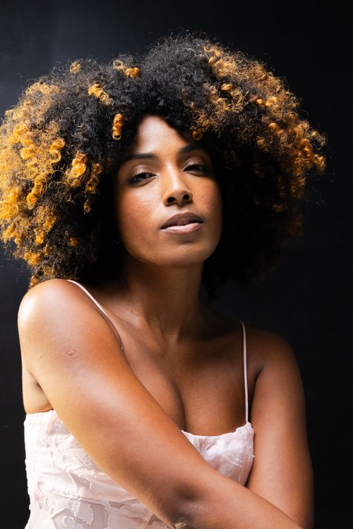 Free Close-up portrait of a confident woman with afro curly hair against a black background. Stock Photo