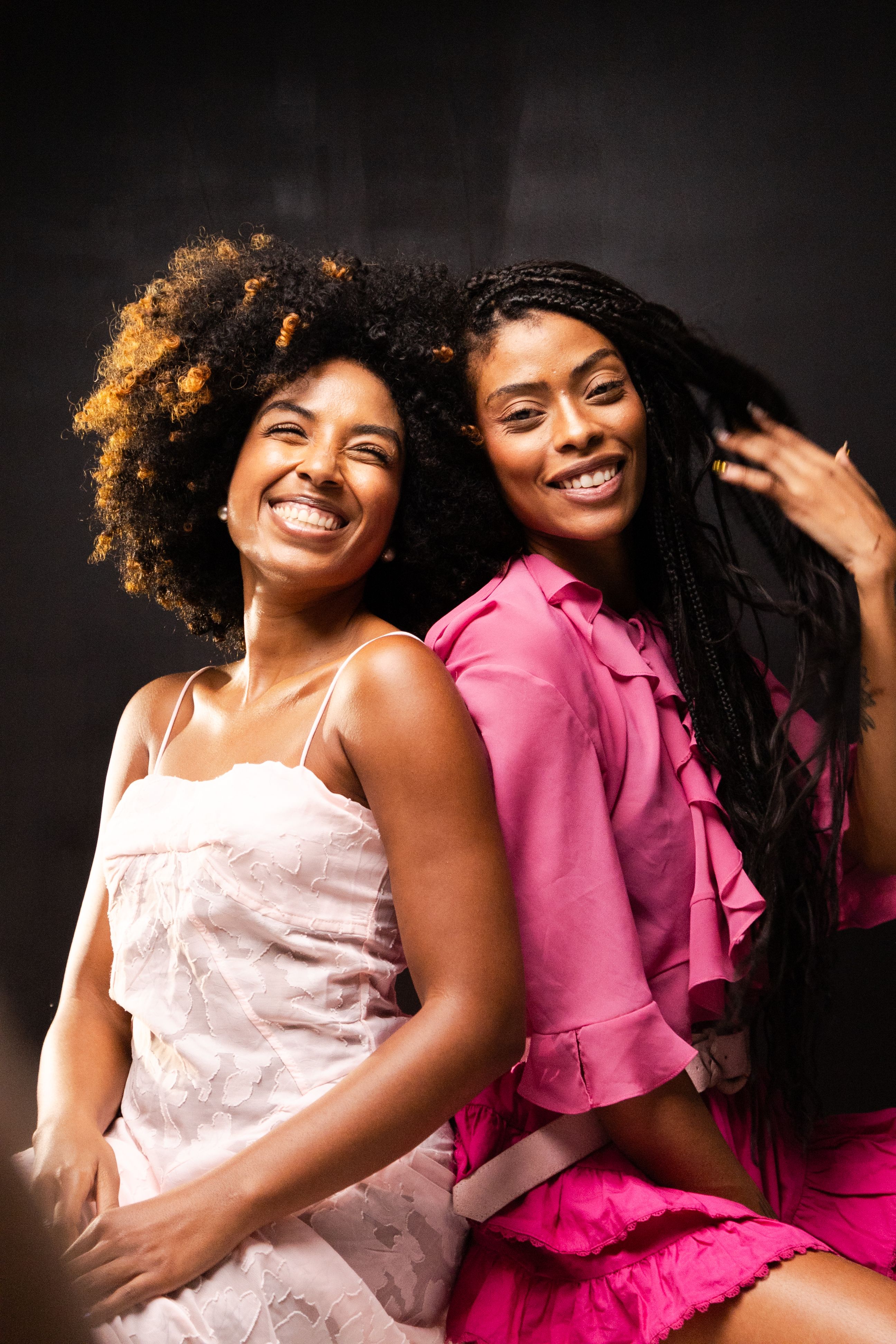 Joyful portrait of two women in fashionable dresses against a dark backdrop, exuding happiness and style.