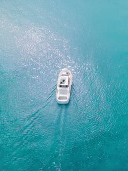 Aerial shot of a white yacht cruising through bright turquoise waters under sunlight.