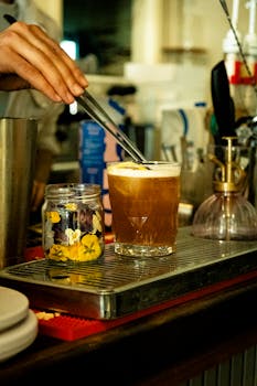 Close-up of a cocktail being crafted in a cozy cafe with floral garnish.
