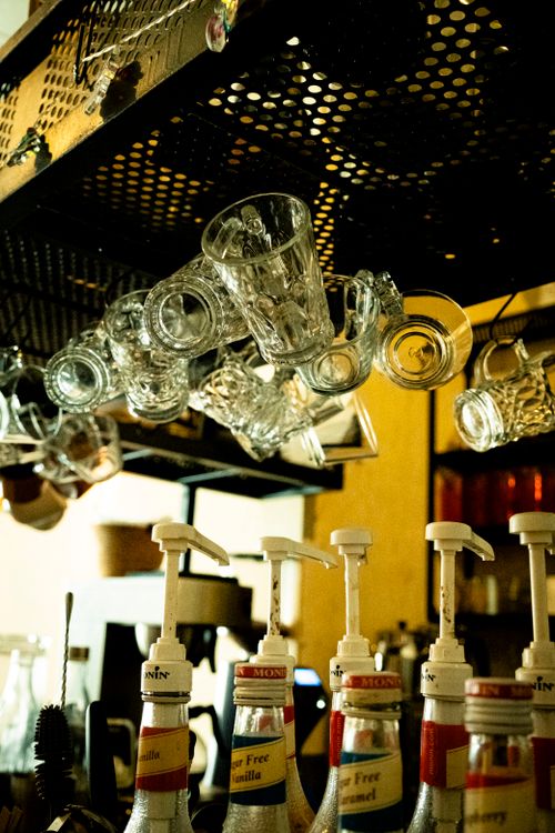 Free Intimate cafe bar setting with hanging glasses and various flavored syrup bottles. Stock Photo