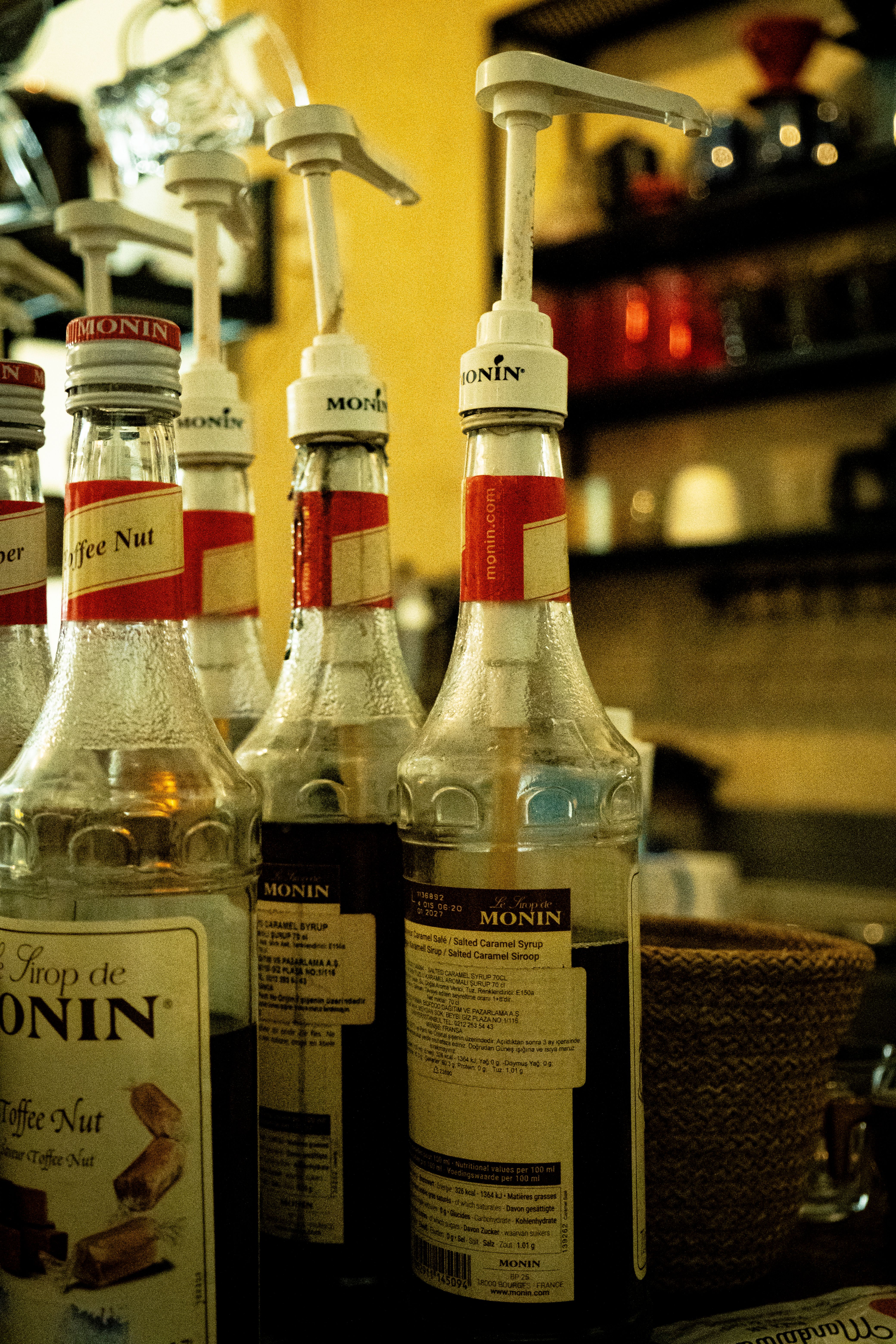 A glass of milk being tinted brown as dark coffee syrup is poured in and stirred, with the syrup bottle beside it