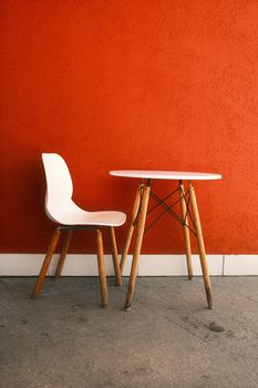 White chair and wooden table set against a vibrant orange wall.