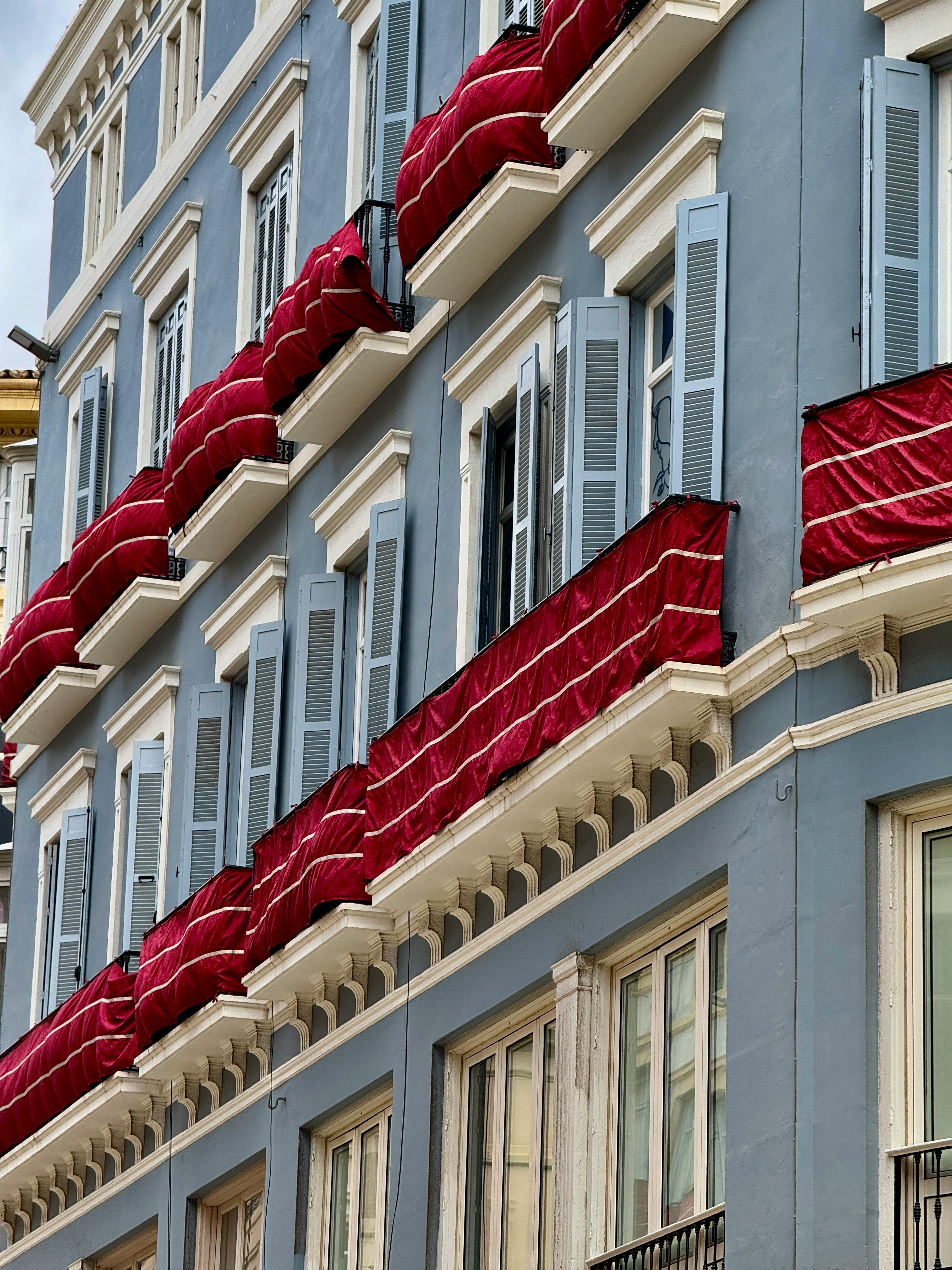 Elegant building facade in Málaga, Spain, featuring vibrant red awnings and classic Mediterranean architecture.