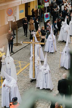 Nazarenos in traditional attire during Holy Week procession in Seville's streets.
