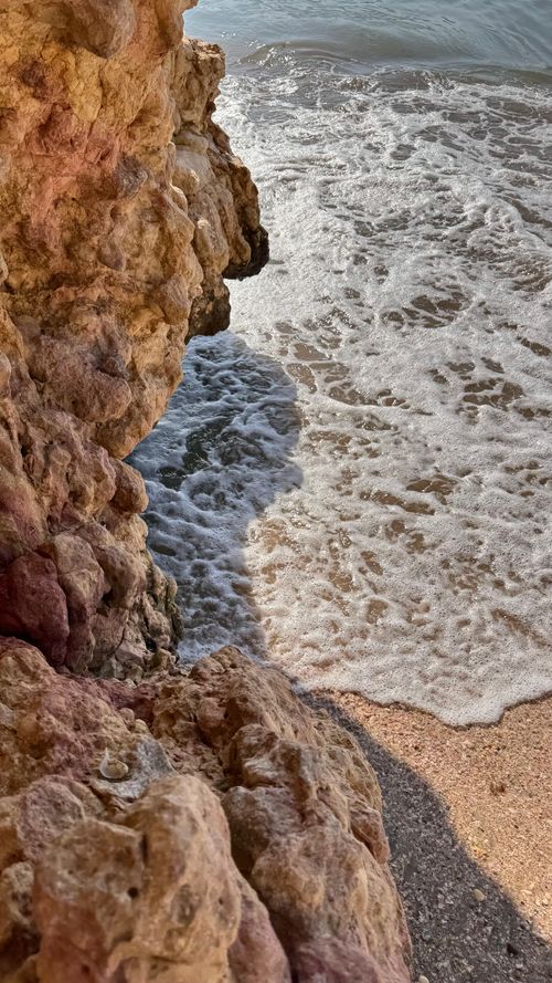 Free Waves gently lap against textured coastal rocks, offering a serene beach scene. Stock Photo