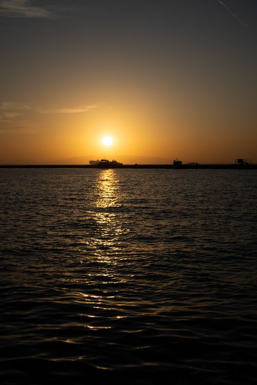 Free A breathtaking sunset casting a warm glow over calm ocean waters with silhouetted ships on the horizon. Stock Photo