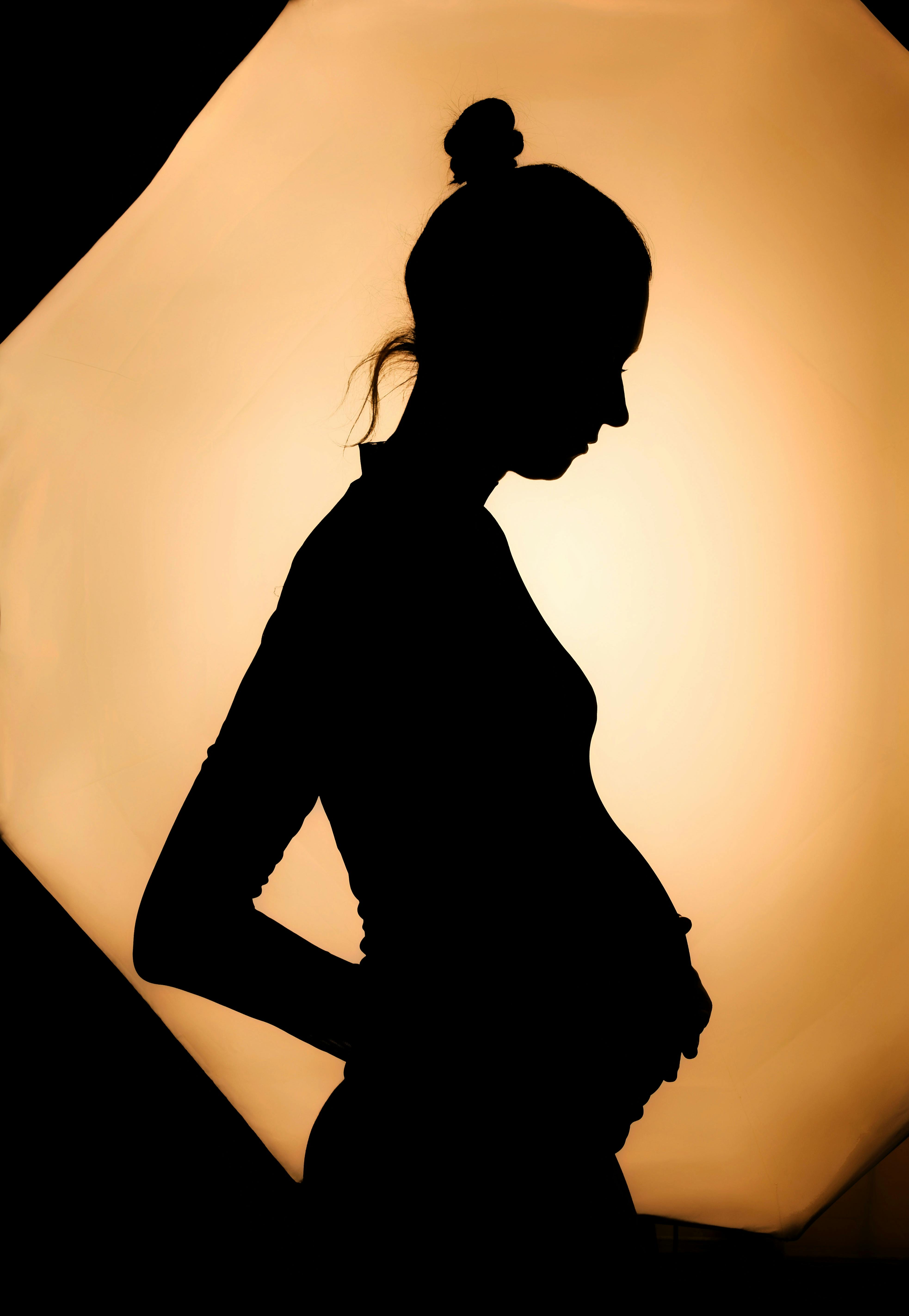 Artistic silhouette of a pregnant woman against warm studio lighting backdrop.