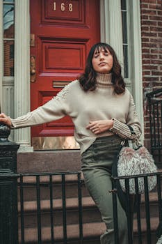 一位穿着舒适毛衣的时尚女子在城镇优雅街道的红门旁摆姿势