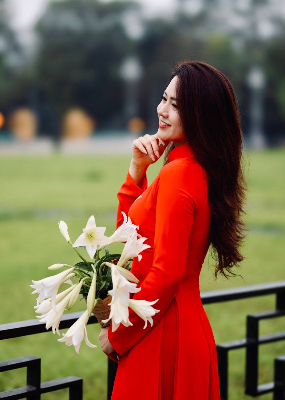 A woman in a red dress holds a bouquet of white lilies, exuding elegance and grace.
