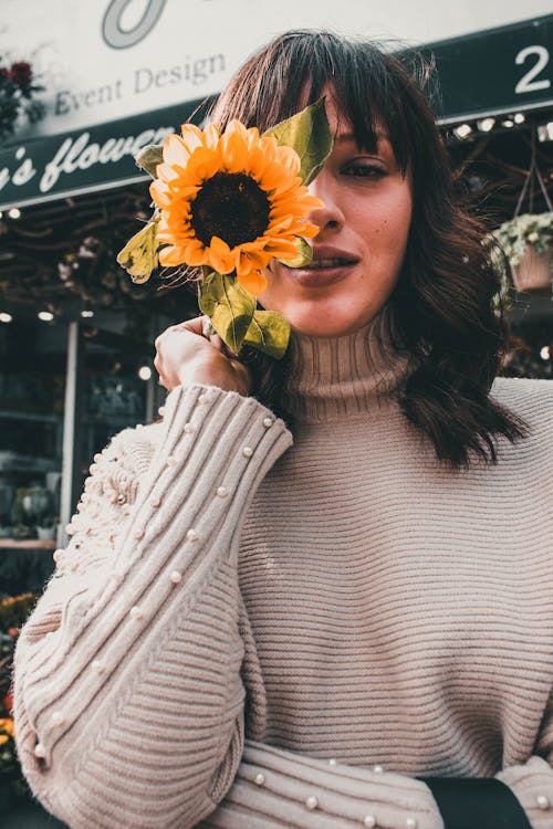 Fotografía De Enfoque Selectivo De Mujer En Suéter Gris Sosteniendo Girasol Amarillo Cerca De Su Rostro