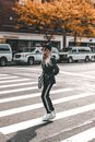 一位穿着黑色服装的时尚女子穿过铺满秋叶的城市街道