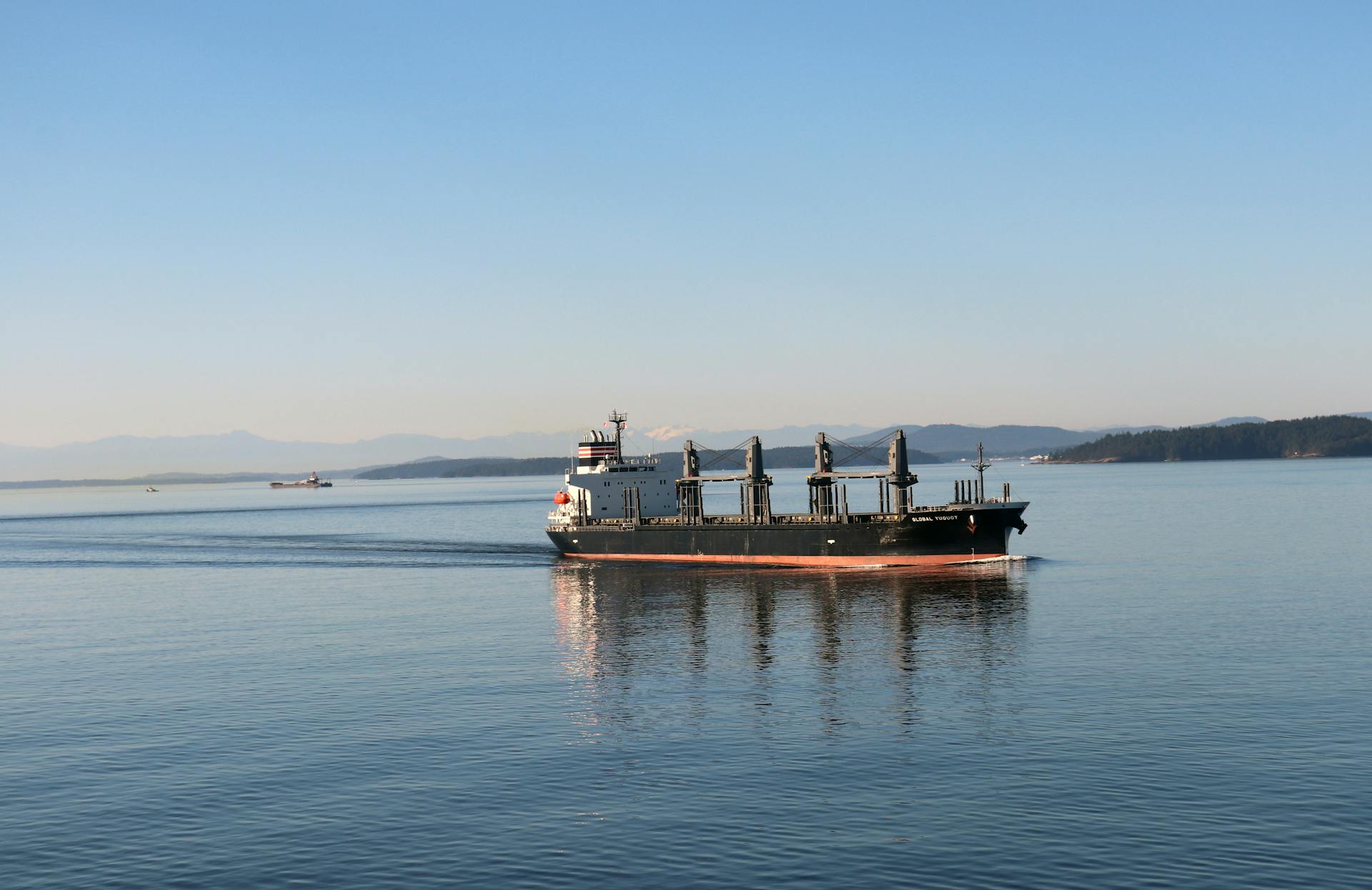 Cargo ship cruising through calm waters with distant mountains in view, during daytime.