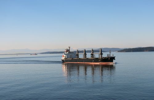 Free Cargo ship cruising through calm waters with distant mountains in view, during daytime. Stock Photo