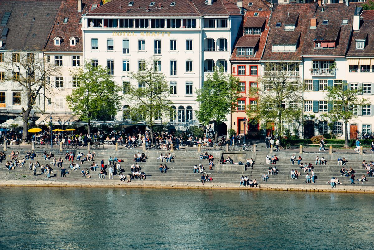 Crowds on the steps of a riverside promenade below tall townhouses