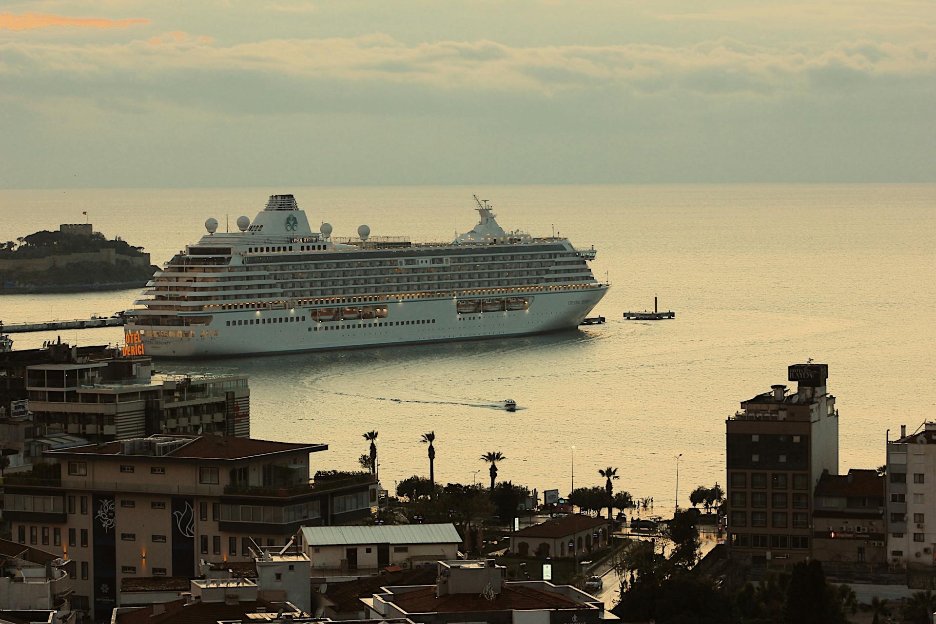 A large cruise ship is docked at a scenic city harbor during daytime.