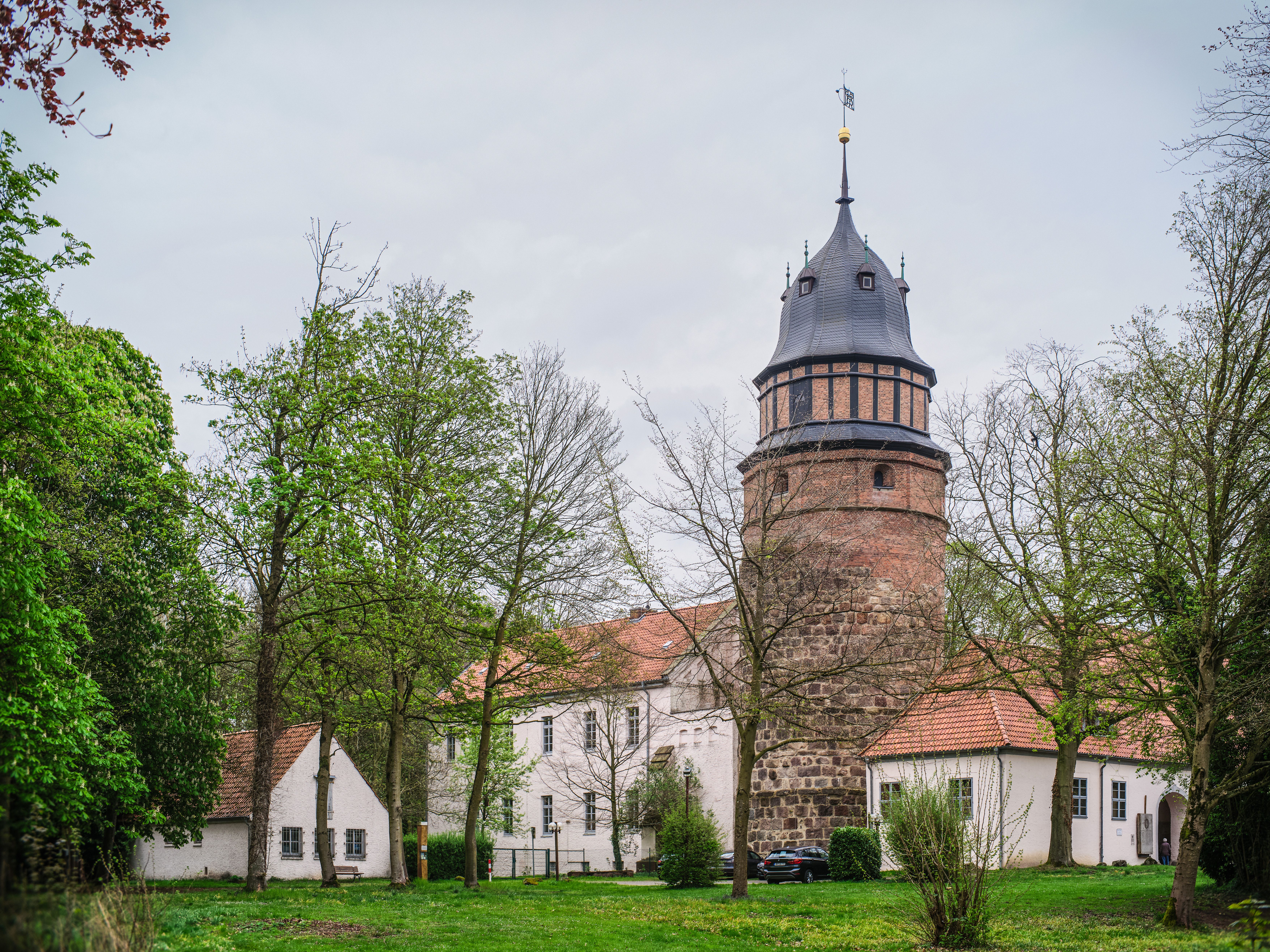 Gratis Storica torre medievale circondata da rigogliosi alberi verdi e palazzi in un sereno ambiente europeo. Foto a disposizione