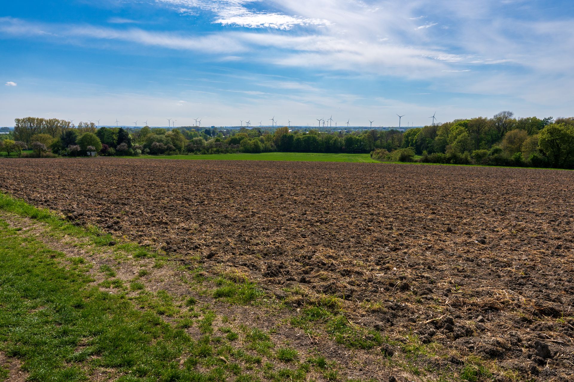 A vast plowed field under a blue sky with distant wind turbines along the horizon.